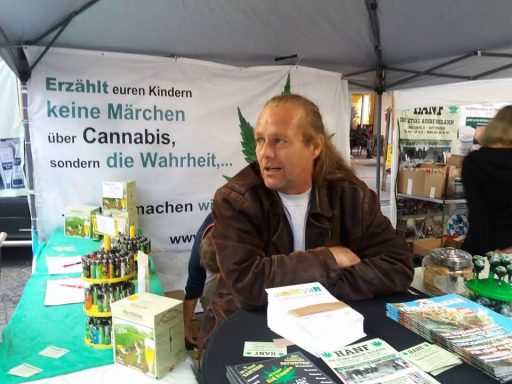 Mann am Stand mit Informationen über Cannabis, umgeben von Produkten und Werbematerialien.